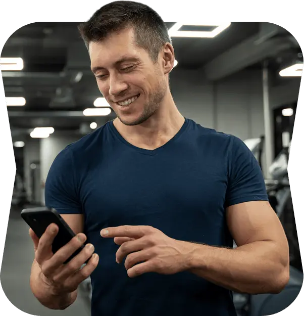 Smiling gym owner in a navy t-shirt checking his phone on the gym floor